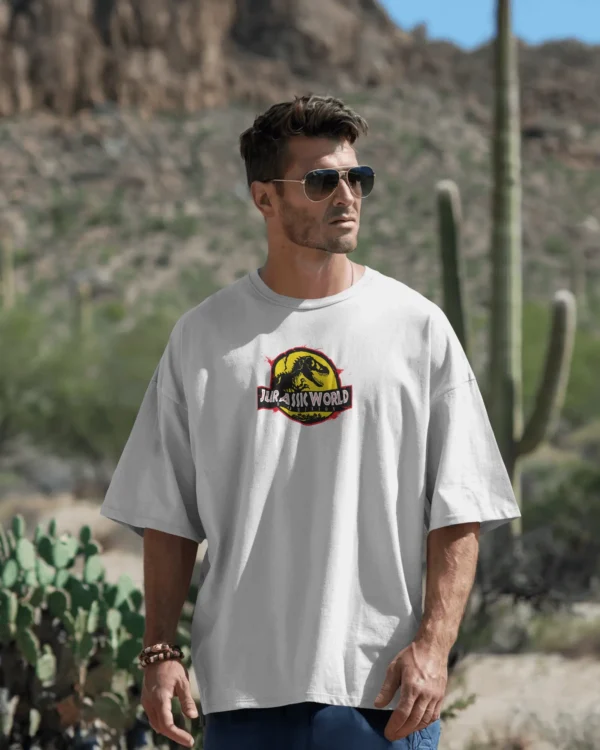 Man wearing an oversized white round neck cotton t-shirt with Jurassic World print, standing outdoors among cacti in a desert setting