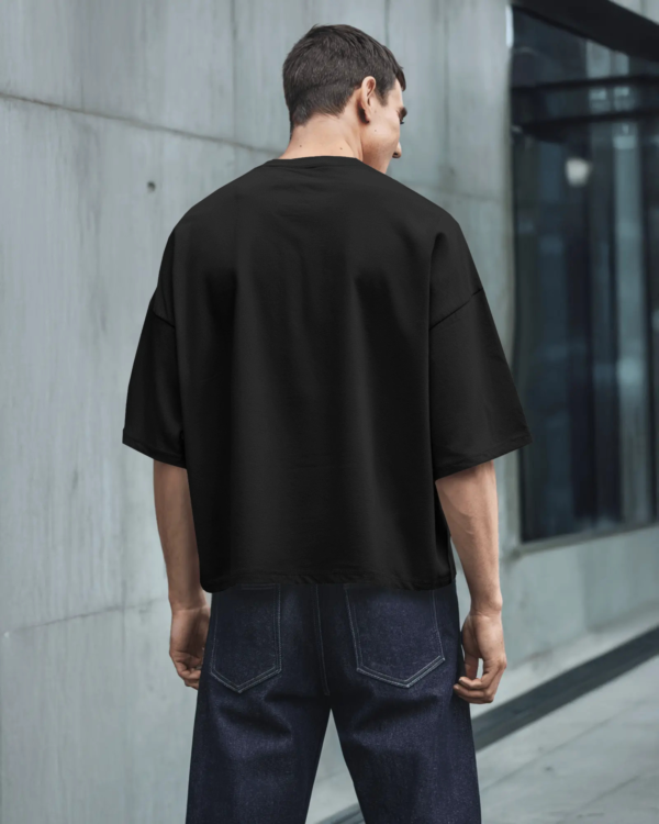 Back view of a male model wearing a black oversized t-shirt and denim in a modern city street setting